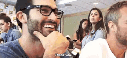 a man with glasses and a beard is smiling and saying `` thank you '' while a woman looks on .