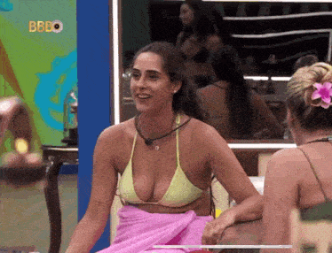 a woman in a bikini sits next to another woman with a flower in her hair and the word bbbo on the bottom