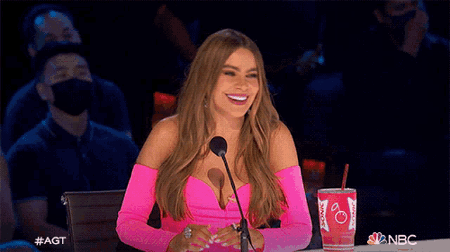 a woman in a pink dress is sitting in front of a microphone with a cup of coca cola in front of her