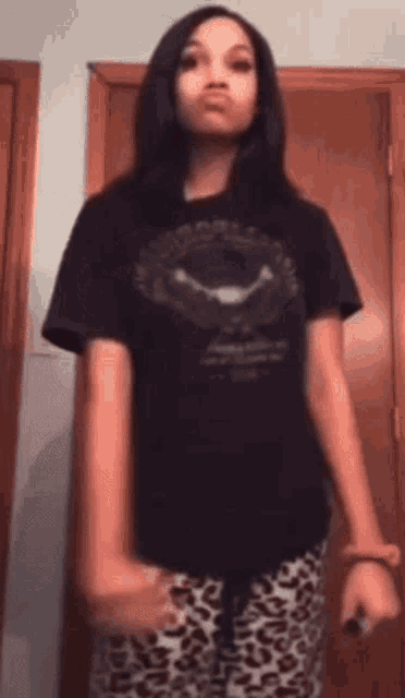 a young girl wearing a black shirt and leopard print pants is standing in front of a door .