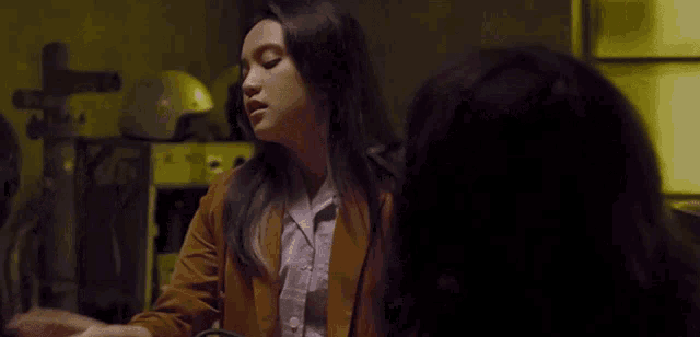 a woman in a brown jacket talking to another woman in a dark room