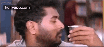 a man with a beard is drinking from a cup and making a funny face .