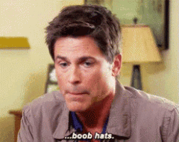 a man is sitting in a living room talking about boobs and hats .