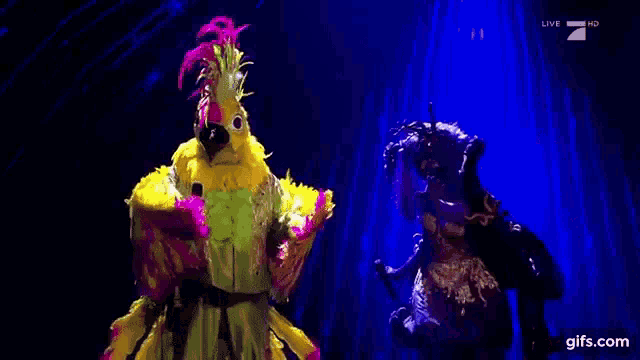 a person dressed as a parrot is standing next to a woman dressed as a parrot on a stage .