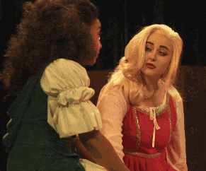 a blonde woman in a red dress talks to another woman in a green dress