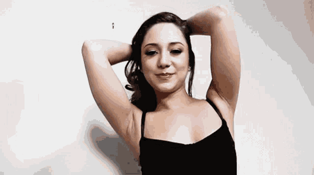 a woman in a black tank top is holding her hair in her hand .