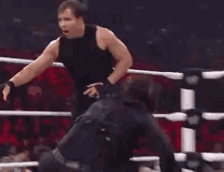 a man in a black tank top is standing in a wrestling ring .