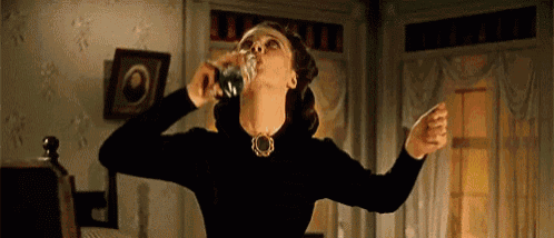 a woman in a black dress is drinking from a bottle .