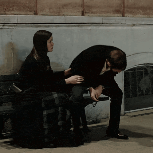 a man and a woman sit on a bench and the woman is touching the man 's arm