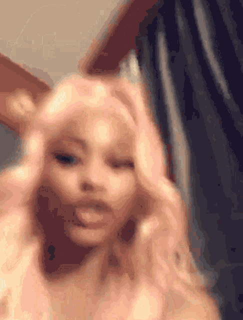 a woman with pink hair is standing in front of a curtain and looking at the camera .