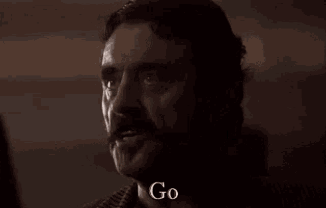 a man with a mustache is saying " yourself " in a dark room .