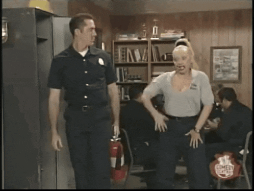 a man and a woman are standing in a room with a fire extinguisher in the foreground
