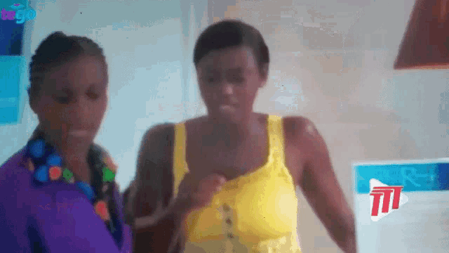 a woman in a yellow tank top stands next to a woman in a purple shirt