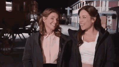 two women are standing next to each other and smiling in front of a horse drawn carriage .