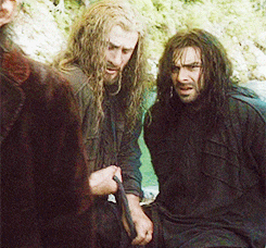 three men with long hair are standing next to each other and one is holding a sword