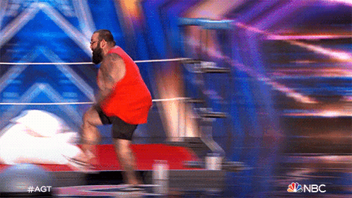 a man in a red tank top and black shorts is jumping in a boxing ring on nbc