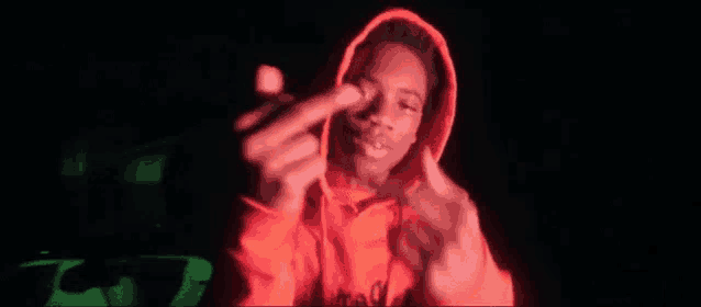 a young man in a red hoodie is giving the middle finger in the dark .