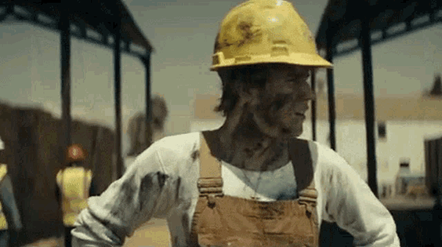 a construction worker wearing a hard hat and overalls is standing in front of a building .