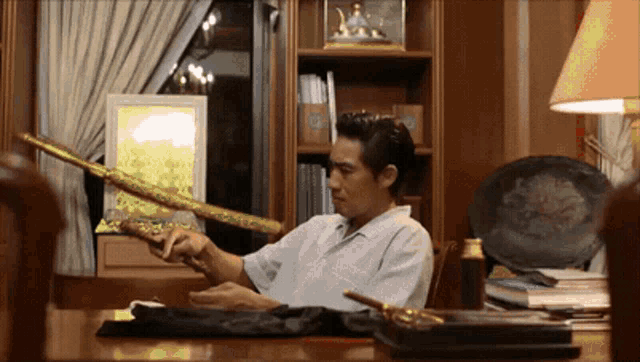 a man sitting at a desk holding a sword with a chinese symbol on it