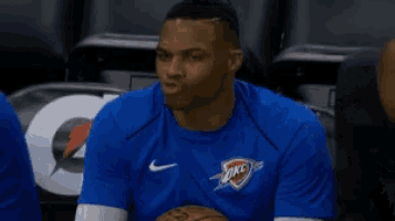 a basketball player wearing a blue shirt is sitting on the bench talking to someone .