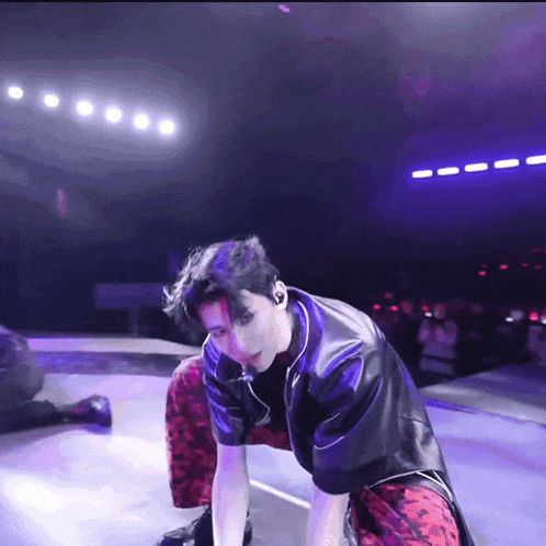 a man in a black leather jacket and red pants is kneeling down on a stage