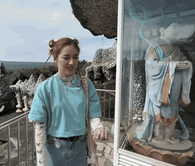 a woman in a blue shirt stands next to a statue of a man