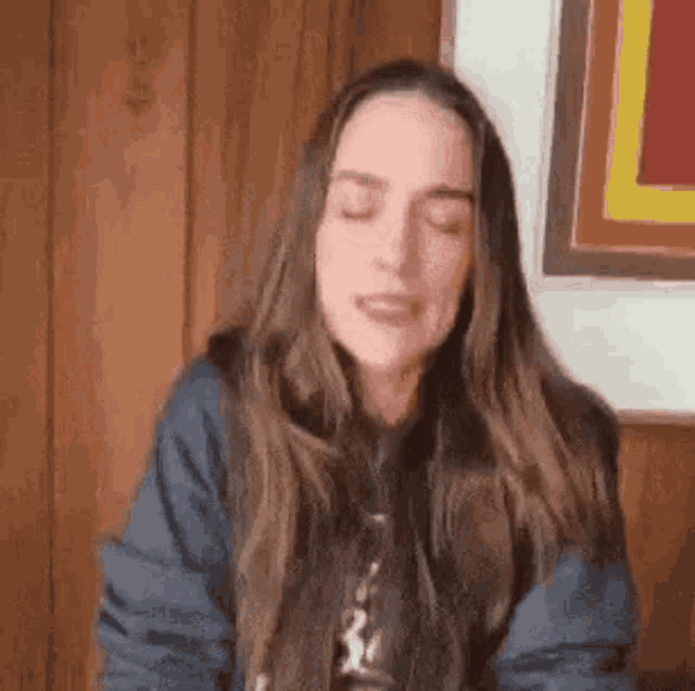 a woman with long brown hair is sitting in front of a wooden wall with her eyes closed .