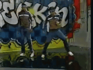 two men are dancing in front of a wall with graffiti on it that says ' rck '