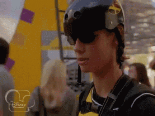 a man wearing a helmet and sunglasses is standing in front of a disney logo .