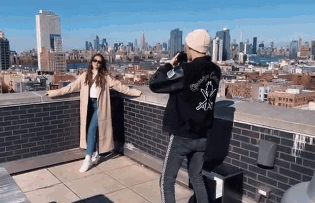 a man is taking a picture of a woman on a rooftop with a city in the background