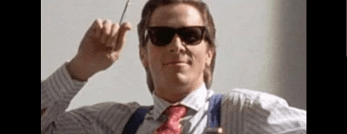 a man wearing sunglasses , suspenders and a tie is holding a pen in his hand .