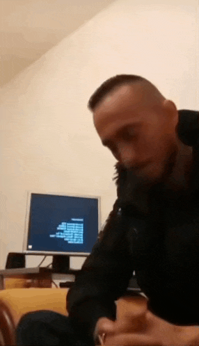 a man in a black jacket is sitting in front of a computer .