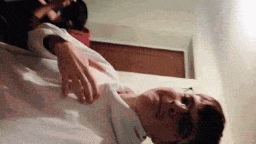 a man with glasses and a white shirt is laying on a bed