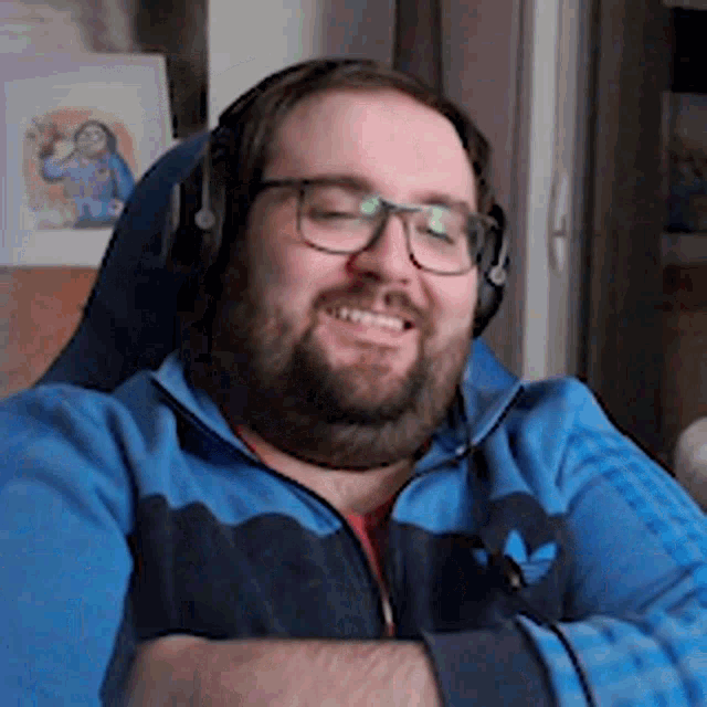 a man wearing headphones and a blue adidas jacket smiles for the camera