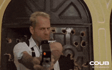 a man holding a gun in front of a door with bullet holes in it .