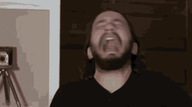 a man with a beard is making a funny face in front of a camera .