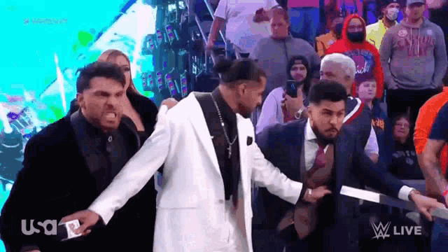 a man in a white suit is being escorted by a man in a black suit and tie .