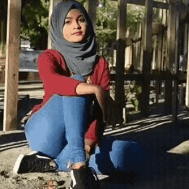 a woman wearing a hijab and jeans is kneeling down on the ground .