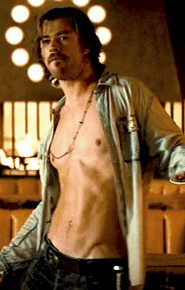 a shirtless man with a necklace around his neck stands in a room