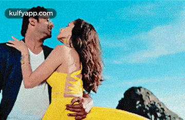 a man is holding a woman in a yellow dress while they are dancing on the beach .