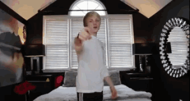 a boy in a white shirt is standing in front of a bed