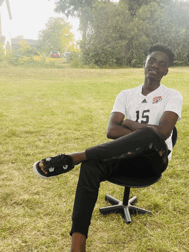 a man wearing a white shirt with the number 15 on it sits on a chair in the grass
