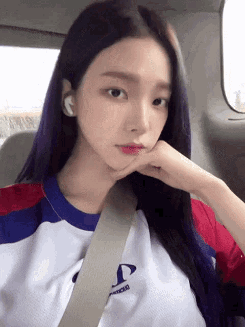 a girl with purple hair is sitting in a car with her hand on her face .