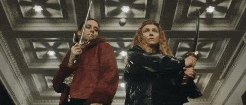 two women standing next to each other holding swords in front of a ceiling