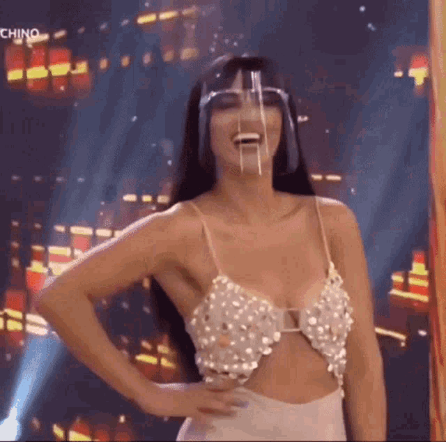 a woman wearing a pearl top and a face shield is standing on a stage .