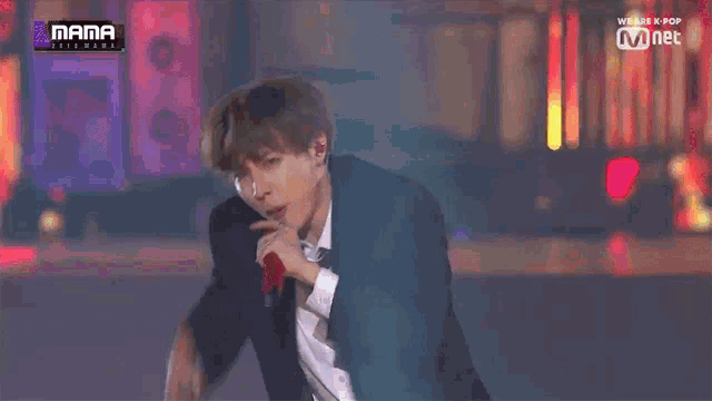 a man in a suit and tie is dancing on a stage with a mnet logo in the background ..