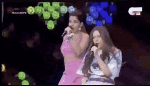 two women are singing into microphones on stage .