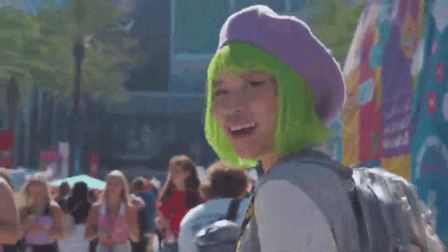 a woman with green hair and a purple hat is walking down a crowded street .
