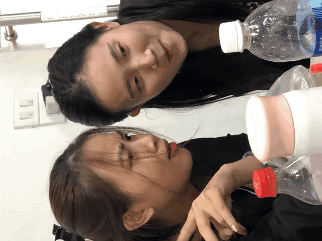 two women are sitting next to each other with a bottle of water in the foreground
