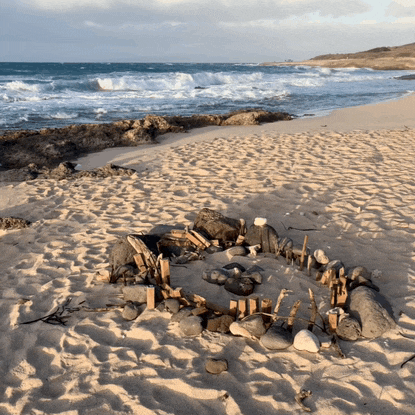 a fire pit on a sandy beach with the ocean behind it